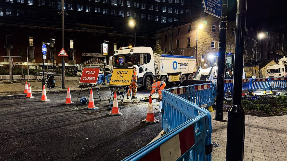 Road workers laying fresh asphalt during a road resurfacing project with machinery nearby.